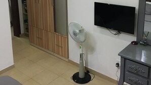 Un soggiorno con televisore, ventilatore, armadio in legno e divano grigio.