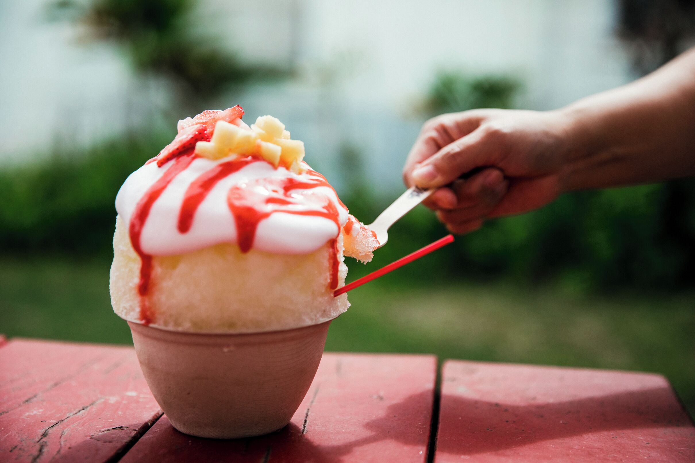 Un tazón de postre de hielo raspado con ingredientes adicionales, sostenido por una mano con una cuchara.