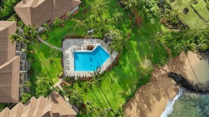Luchtbeeld van een resort met een centraal gelegen zwembad, palmbomen en een strand.