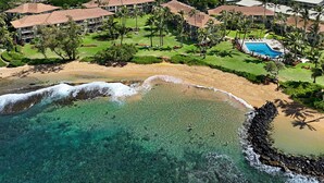 Luchtbeeld van een resort met een strand, helder turquoise water en een zwembad omringd door palmbomen.