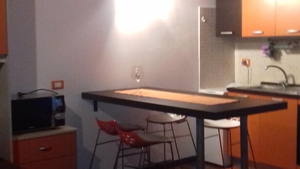 A compact kitchen with a dining area, wooden cabinets, and a small bar stool. - Ghirla lake. Studio flat (Ghirla)