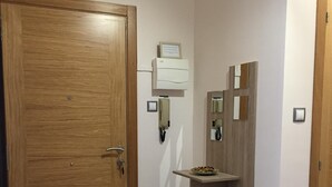 A hallway with a wooden door, a wall-mounted telephone, and a shelf with a bowl of fruit.