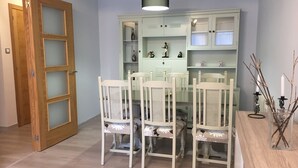 A dining area with a white table and chairs, a light blue wall, and a wooden door with glass panels.