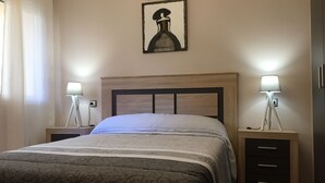 A neatly made bed with a patterned bedspread, two bedside tables with lamps, a headboard, and a framed artwork on the wall.