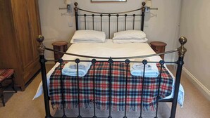 Cama com estrutura de metal, duas almofadas, manta xadrez e cabeceira com luminárias fixadas na parede.