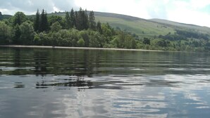 Um lago tranquilo com reflexos de árvores e colinas ao fundo.