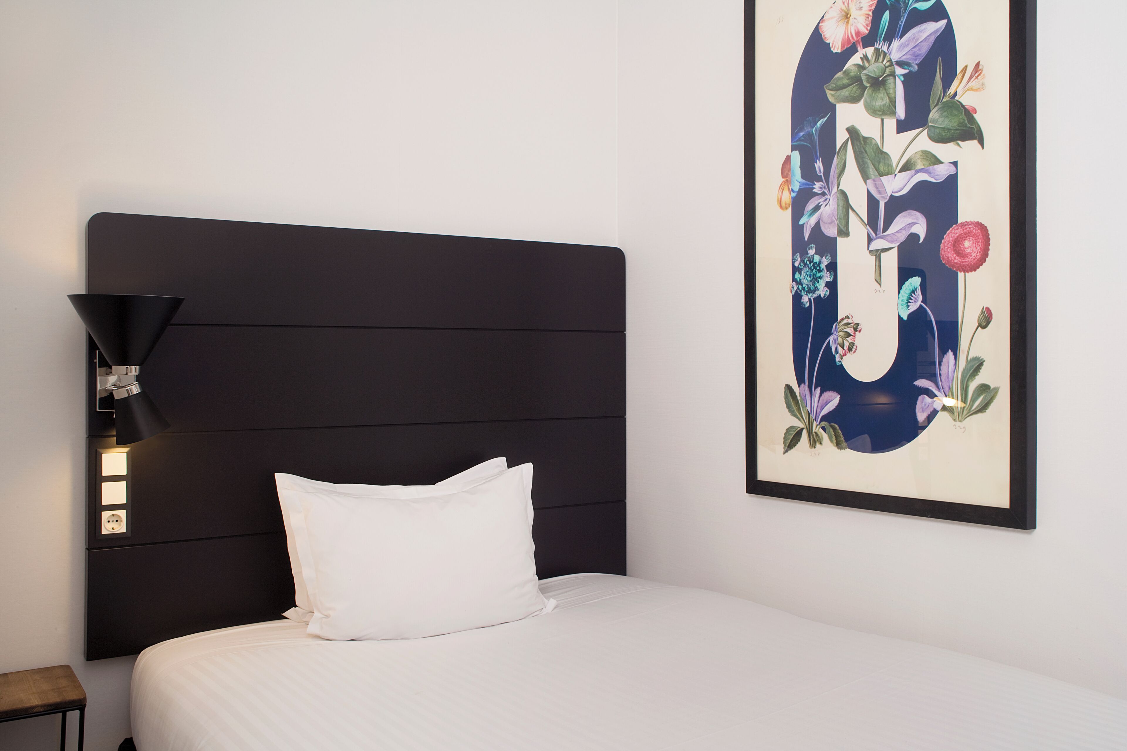 A neatly made bed with white bedding, a dark headboard, and a wall-mounted light fixture.