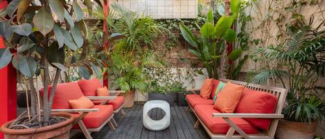 An outdoor patio with wooden furniture, potted plants, and a brick wall.
