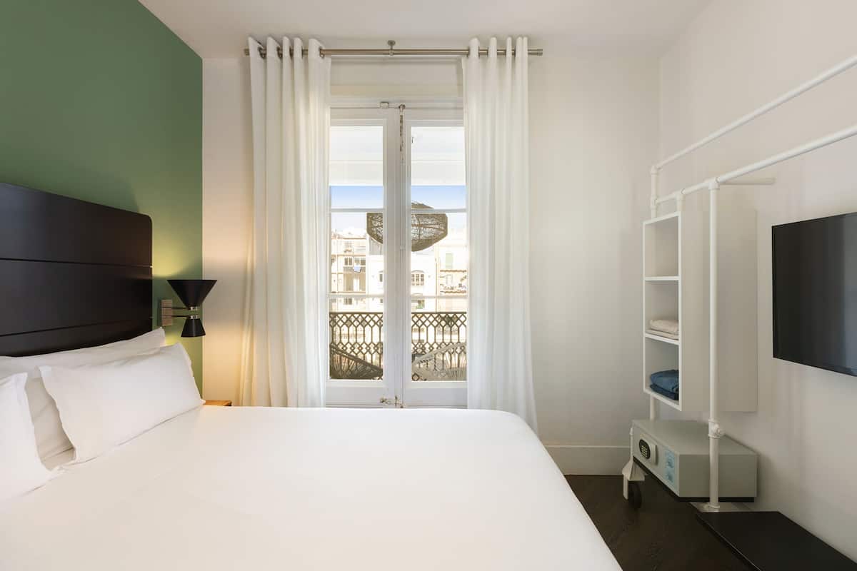 Une chambre d’hôtel avec un lit, une télévision, un petit bureau et un balcon avec vue.