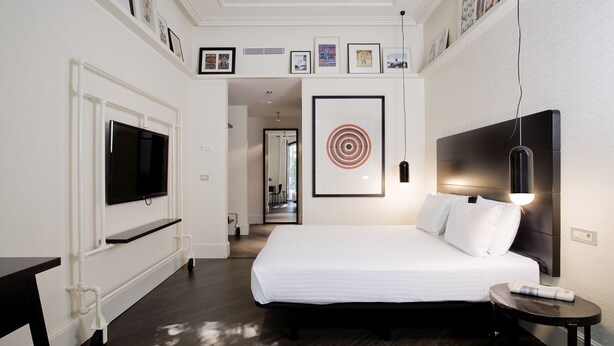 A hotel room with a large bed, a flat-screen TV mounted on the wall, a bedside table with a lamp, and a small table with a remote control. - Hotel Praktik Garden (Barcelona)