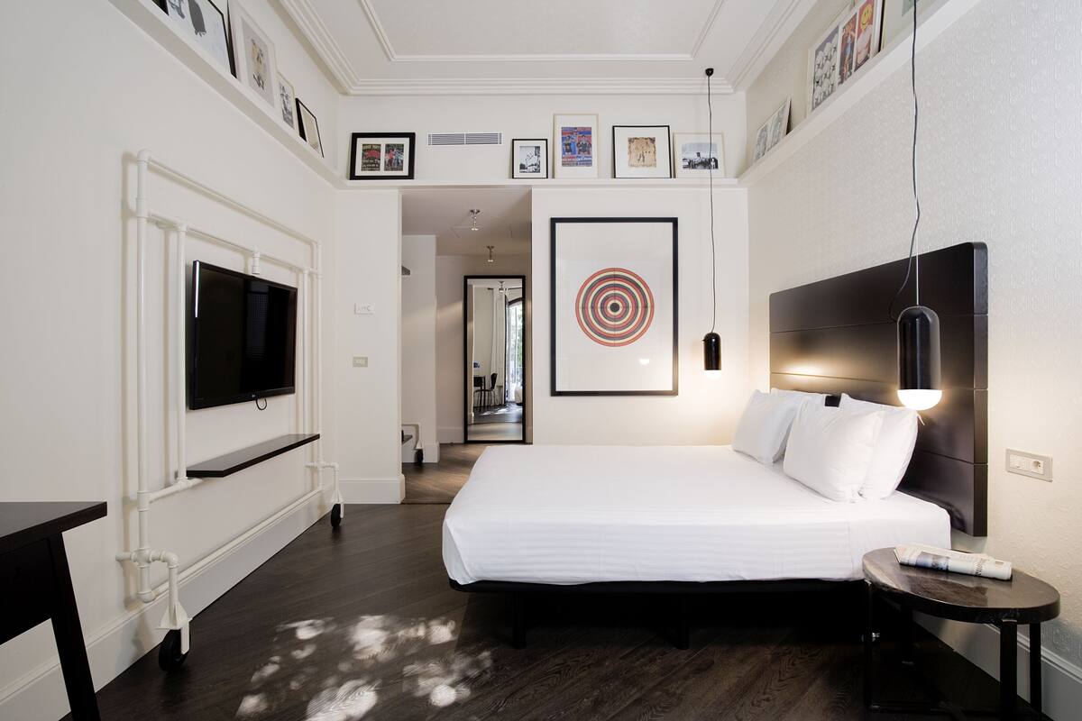 Une chambre d’hôtel avec un grand lit, un téléviseur à écran plat fixé au mur, une table de chevet avec une lampe et une petite table avec une télécommande.