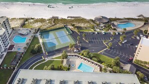 Luchtbeeld van een resort met meerdere zwembaden, een strand en een parkeerplaats.
