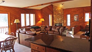 Interior acogedor de una cabaña con chimenea de piedra, paredes de madera, un sofá de cuero y una zona de comedor.