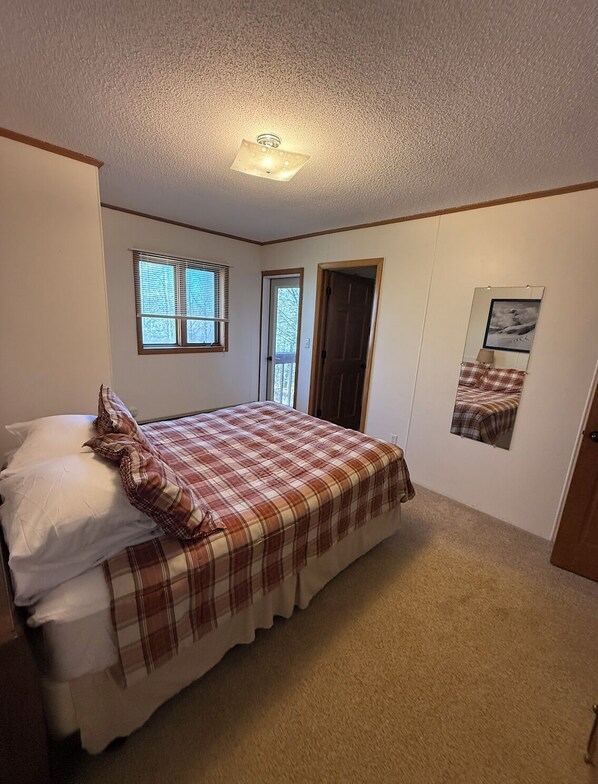 Une chambre à coucher avec un lit, une fenêtre, une porte et un miroir fixé au mur.