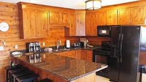 Una cocina con armarios de madera, un refrigerador negro, una cafetera y un lavaplatos.