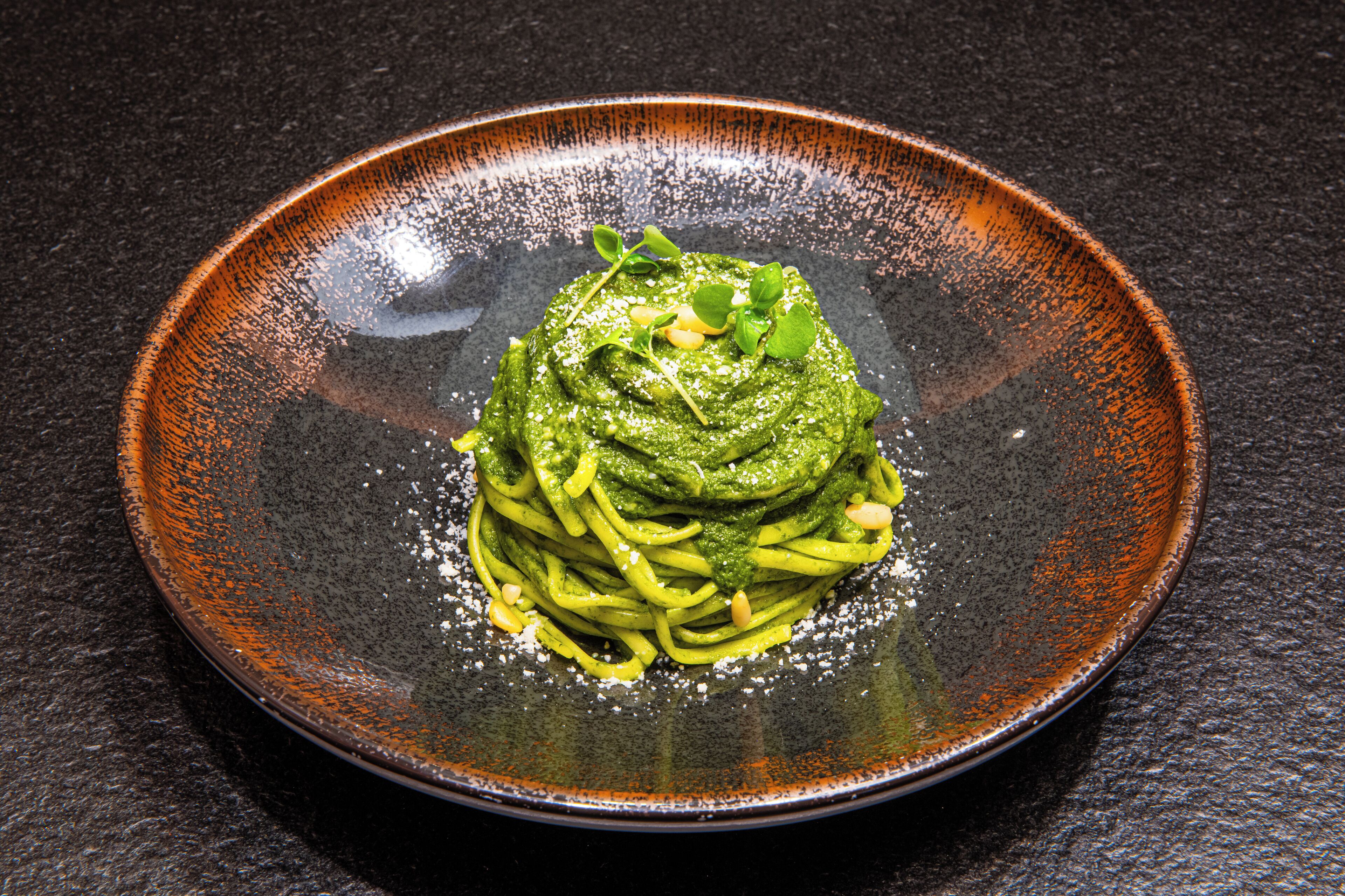 A plate of pasta with a green sauce and garnish on a dark, textured surface.