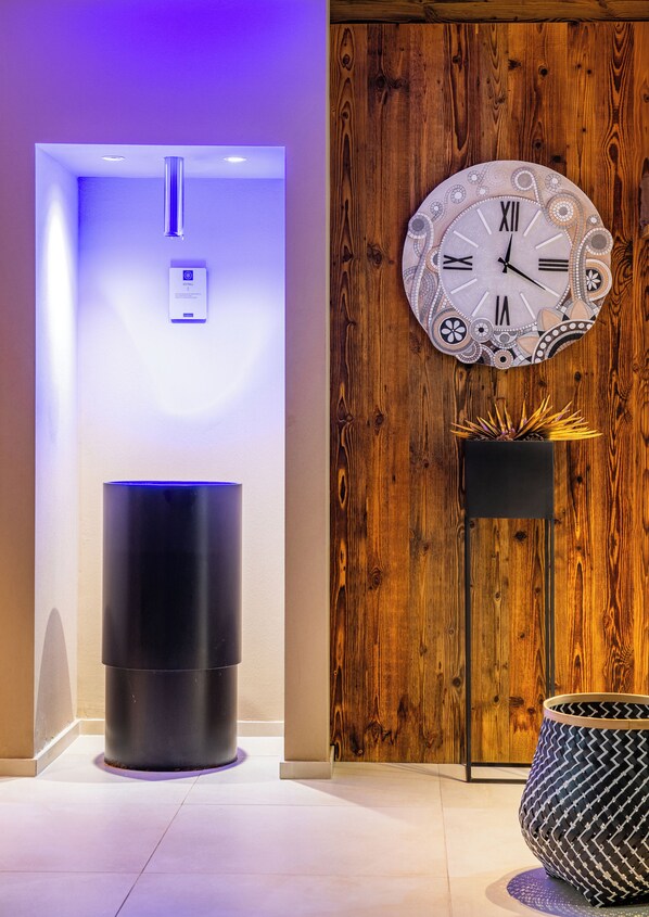 A modern lobby with a wooden wall, a decorative clock, a black cylindrical object, and a patterned floor lamp.