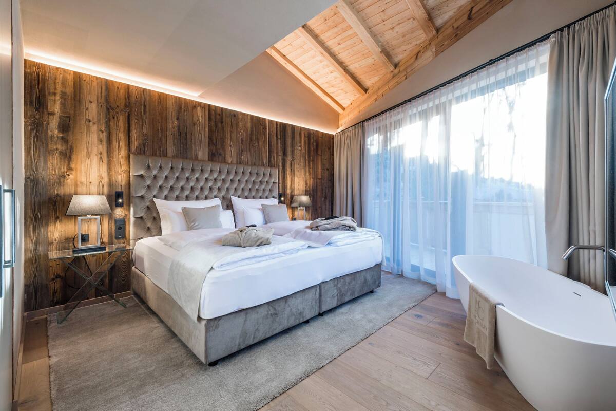 Un dormitorio moderno con una cama grande, paneles de madera, un tragaluz, un baño con bañera y vistas al exterior.