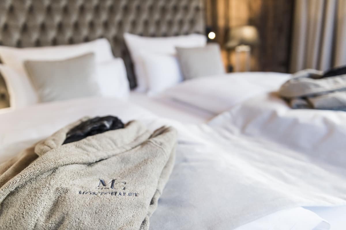 Habitación de hotel con una cama bien hecha, una bata sobre la cama y un cabecero con diseño capitonado.