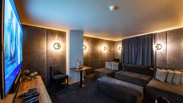 A modern hotel room with a large flat-screen TV, a sofa, a small table, and a chair.