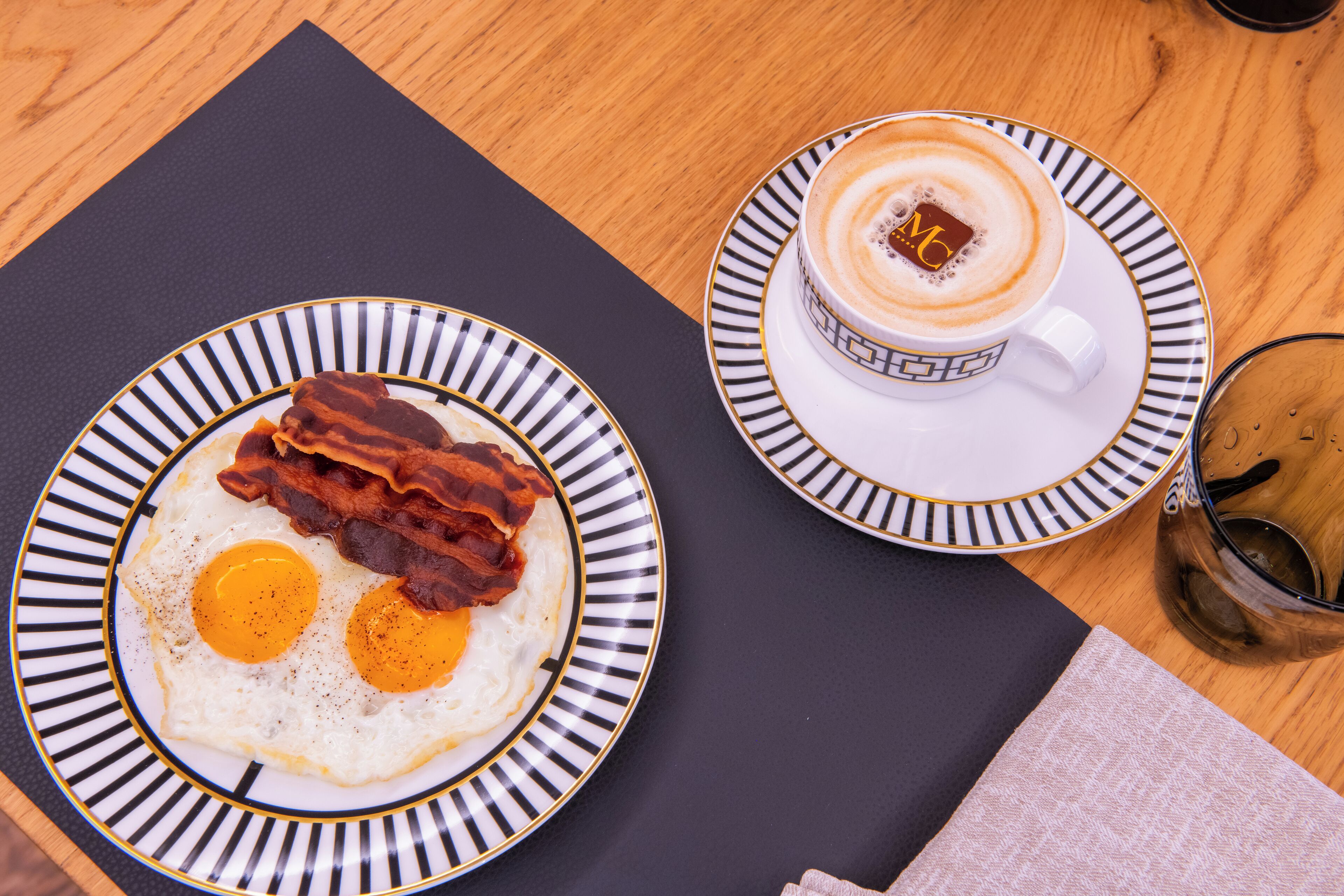 Ett frukostbord med en tallrik ägg och bacon, en kopp kaffe och ett glas vatten.