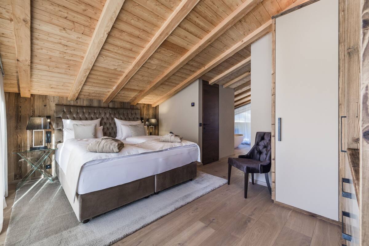 Un dormitorio con una cama grande, vigas de madera en el techo, una mesa de vidrio y una silla.