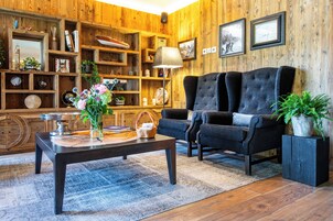 Una sala de estar acogedora con una pared de madera, un sofá oscuro, una mesa de centro y estanterías llenas de libros y objetos decorativos.
