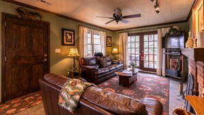 A cozy living room with a leather sofa, a wooden door, and a fireplace. - Bear Bungalow - 1 mile from Main Street Blowing Rock! Hot Tub - Pet Friendly - Fenced In Yard (Blowing Rock)
