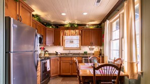 A kitchen with wooden cabinets, a stainless steel refrigerator, a microwave, and a dining table with chairs. - Bear Bungalow - 1 mile from Main Street Blowing Rock! Hot Tub - Pet Friendly - Fenced In Yard (Blowing Rock)