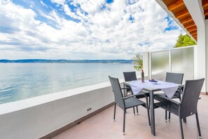 Ein Balkon mit Tisch und Stühlen mit Blick auf ein Gewässer und hügelige Landschaft in der Ferne.