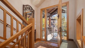 Un escalier en bois mène à une porte vitrée donnant sur une terrasse en bois et des arbres.
