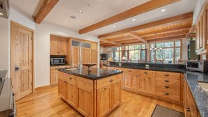Une cuisine spacieuse dotée de meubles en bois, d’un grand îlot central et offrant une vue sur l’extérieur grâce à de grandes fenêtres.