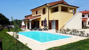 Una casa de dos pisos con piscina, mobiliario exterior y zona de barbacoa.