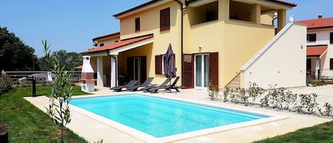 A two-story house with a swimming pool, outdoor seating, and a barbecue area.