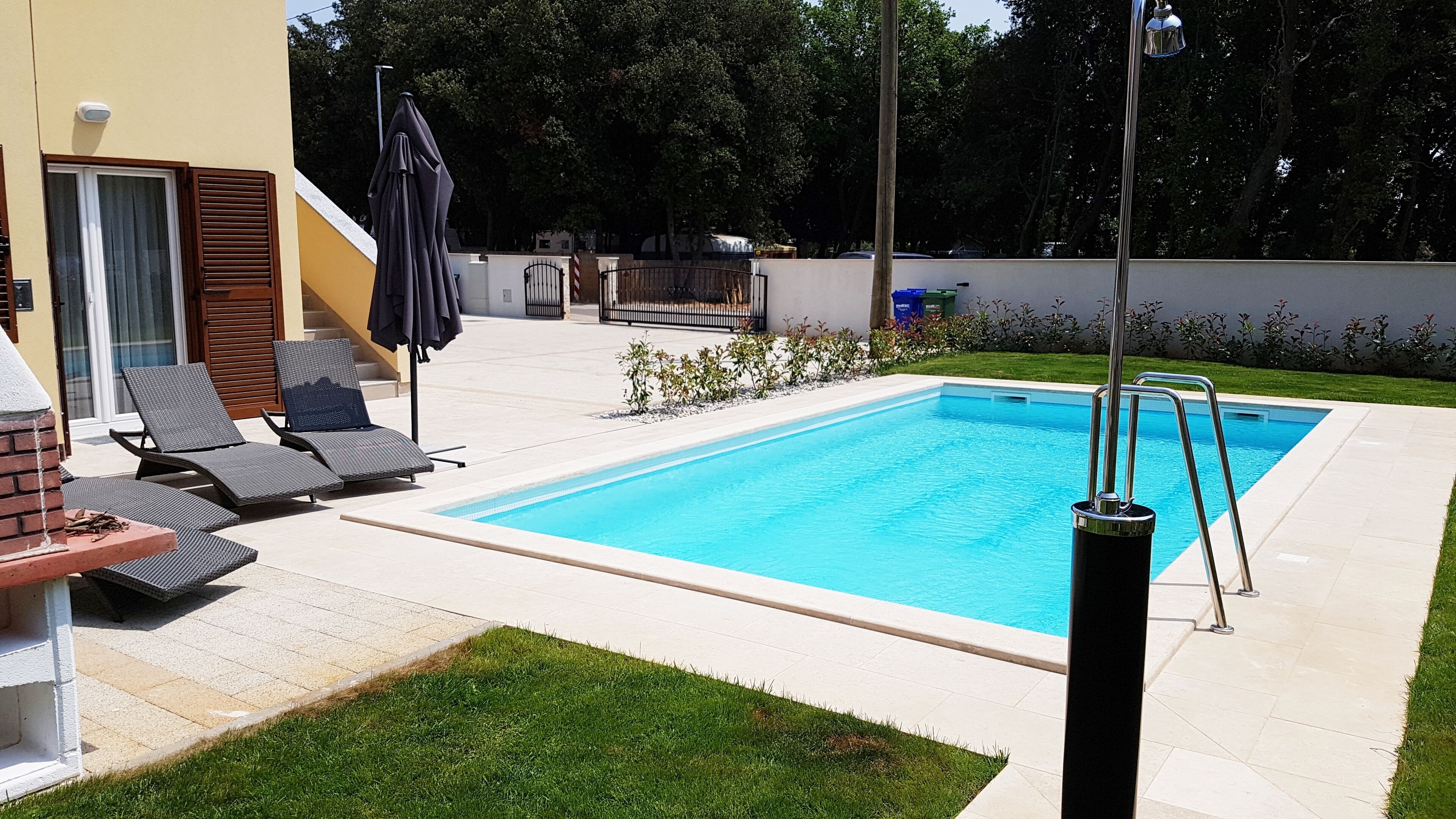 Une piscine rectangulaire à l’eau d’un bleu limpide, entourée d’une terrasse dallée avec des chaises longues et une petite construction en briques.
