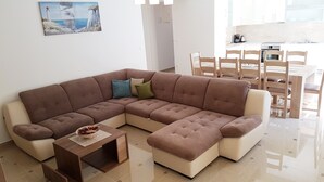 Una sala de estar moderna con un sofá seccional, una pequeña mesita de madera y un comedor con sillas y una mesa de madera.