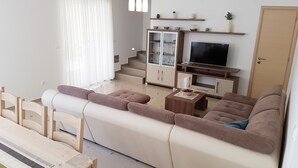 Una sala de estar moderna con un sofá, una mesa de centro y un televisor. Se ve una escalera que sube a un nivel superior.