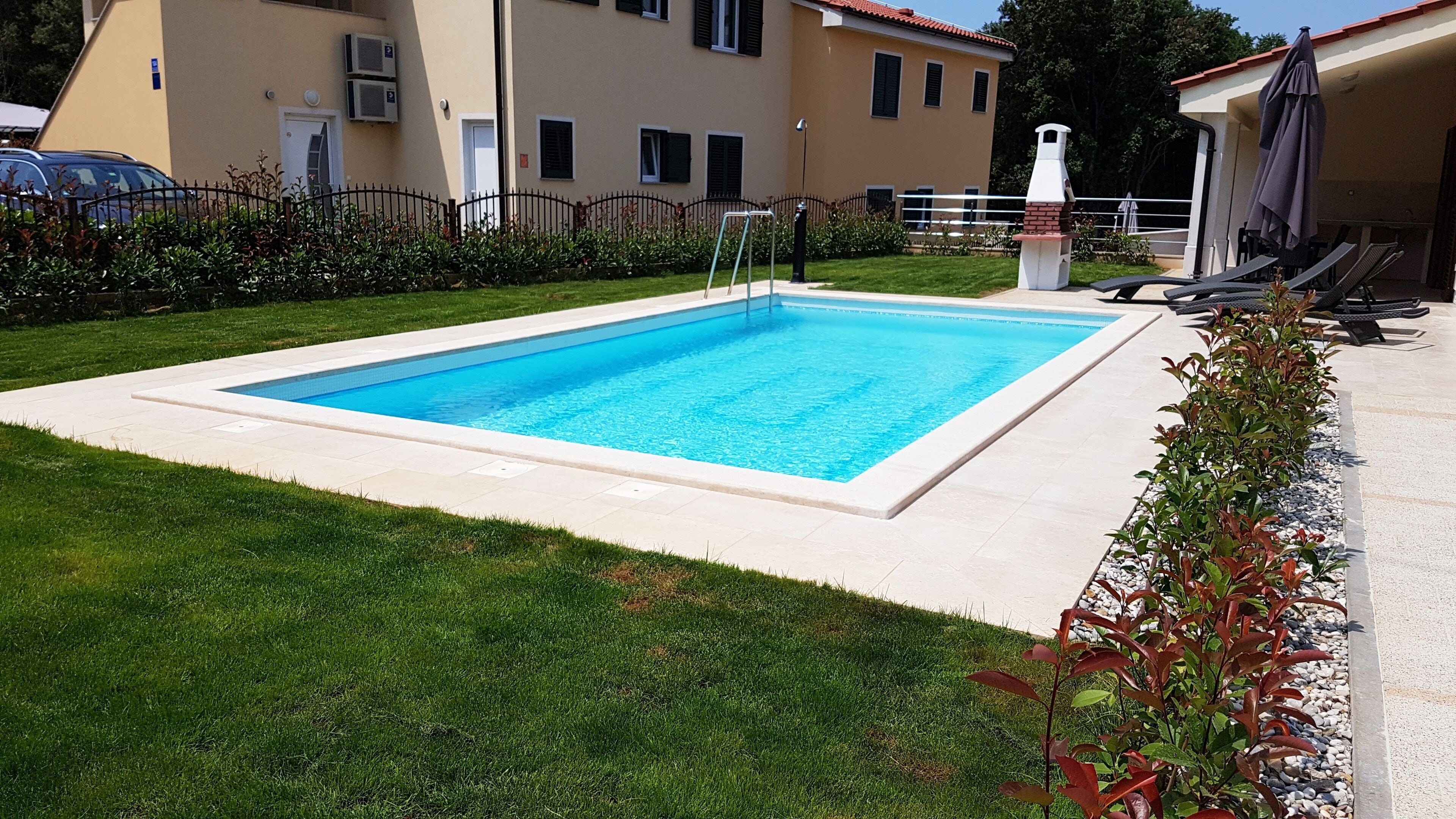 A rectangular swimming pool with a tiled edge, surrounded by a grassy lawn and a low brick wall.