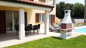 Un espacio al aire libre techado con mesa y sillas, una parrilla y una piscina.