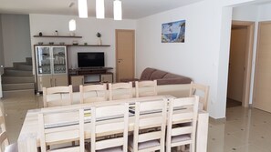 Una sala de estar moderna con comedor, televisor y una escalera que sube a otro nivel.