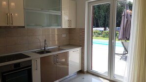Una cocina moderna con horno integrado, un fregadero y ventana con vista a una piscina.