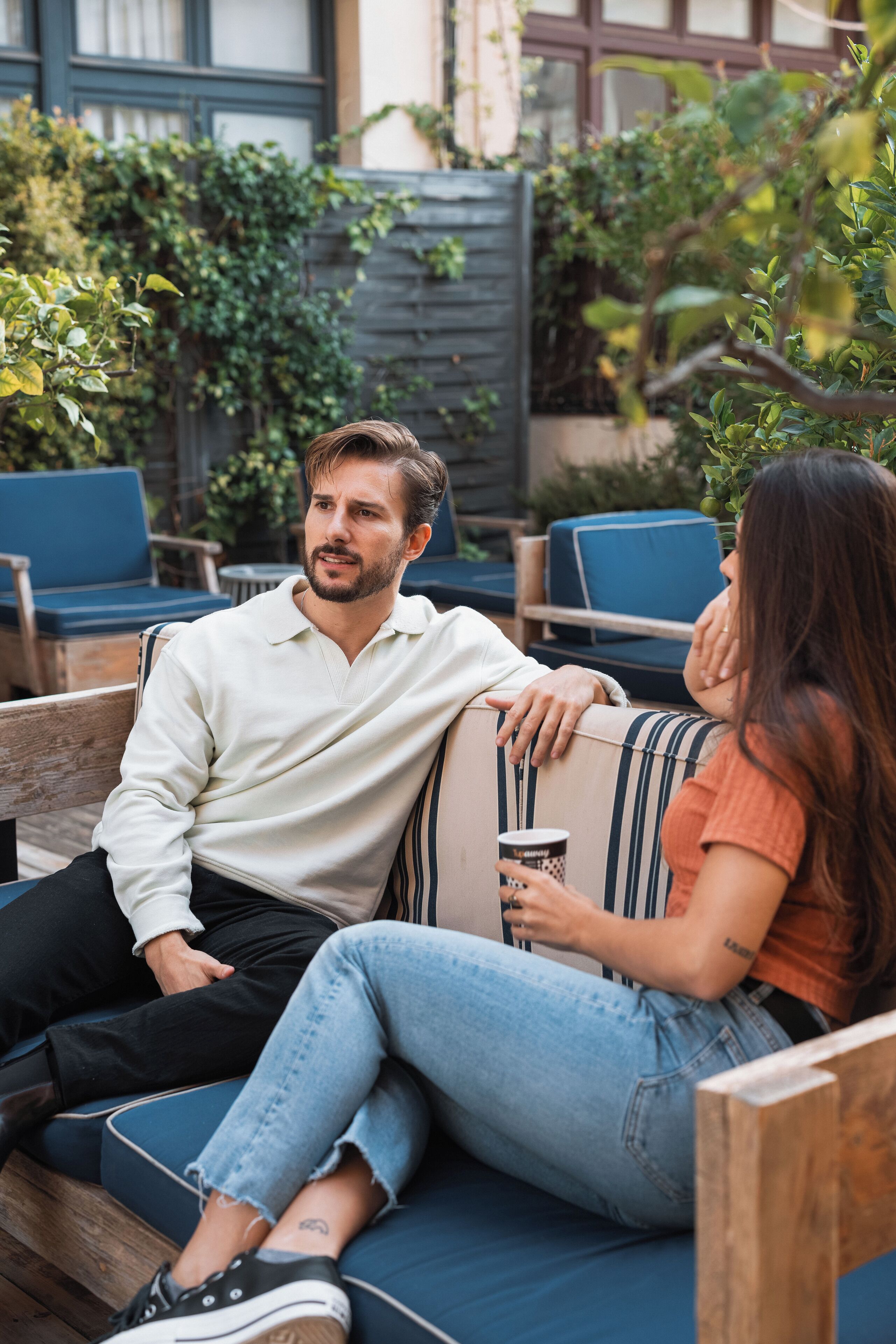 A couple sitting on a blue outdoor sofa with a wooden table and chairs nearby.
