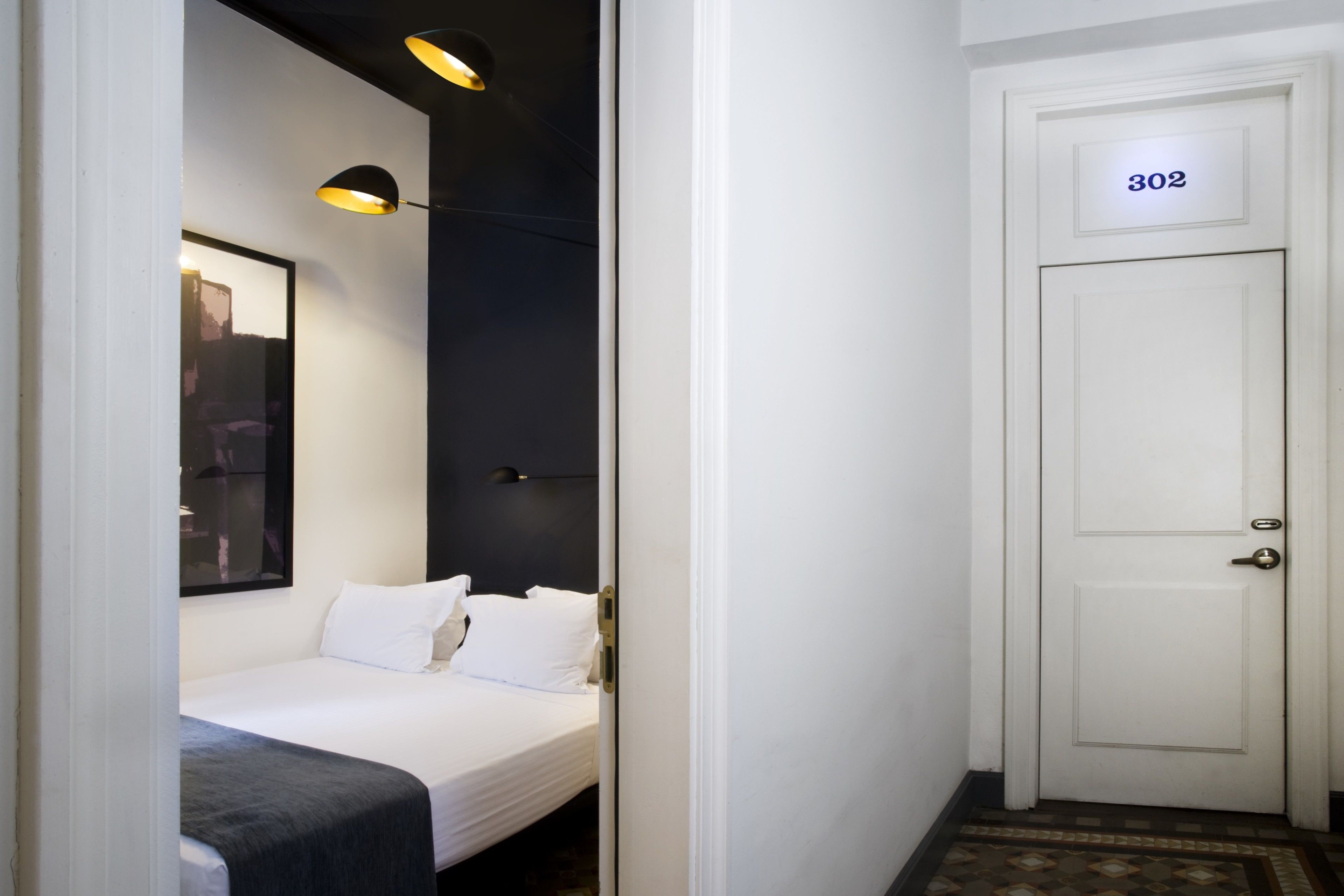 A hotel room with a bed, a door with the number 302, and a hallway with a patterned floor.