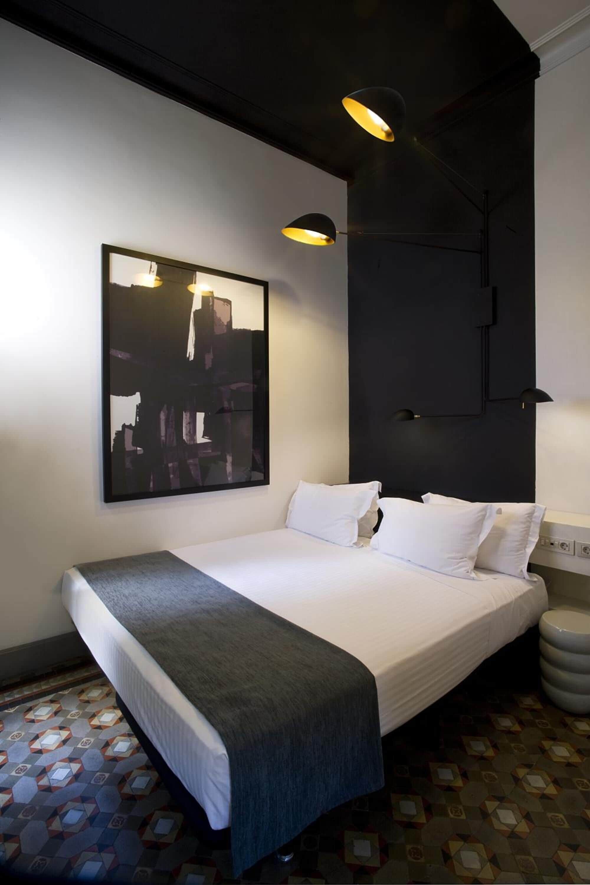 A modern hotel room with a neatly made bed, a large abstract painting on the wall, and a unique geometric patterned floor.