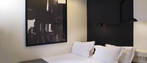 A modern hotel room with a neatly made bed, a large abstract painting on the wall, and a unique geometric patterned floor.