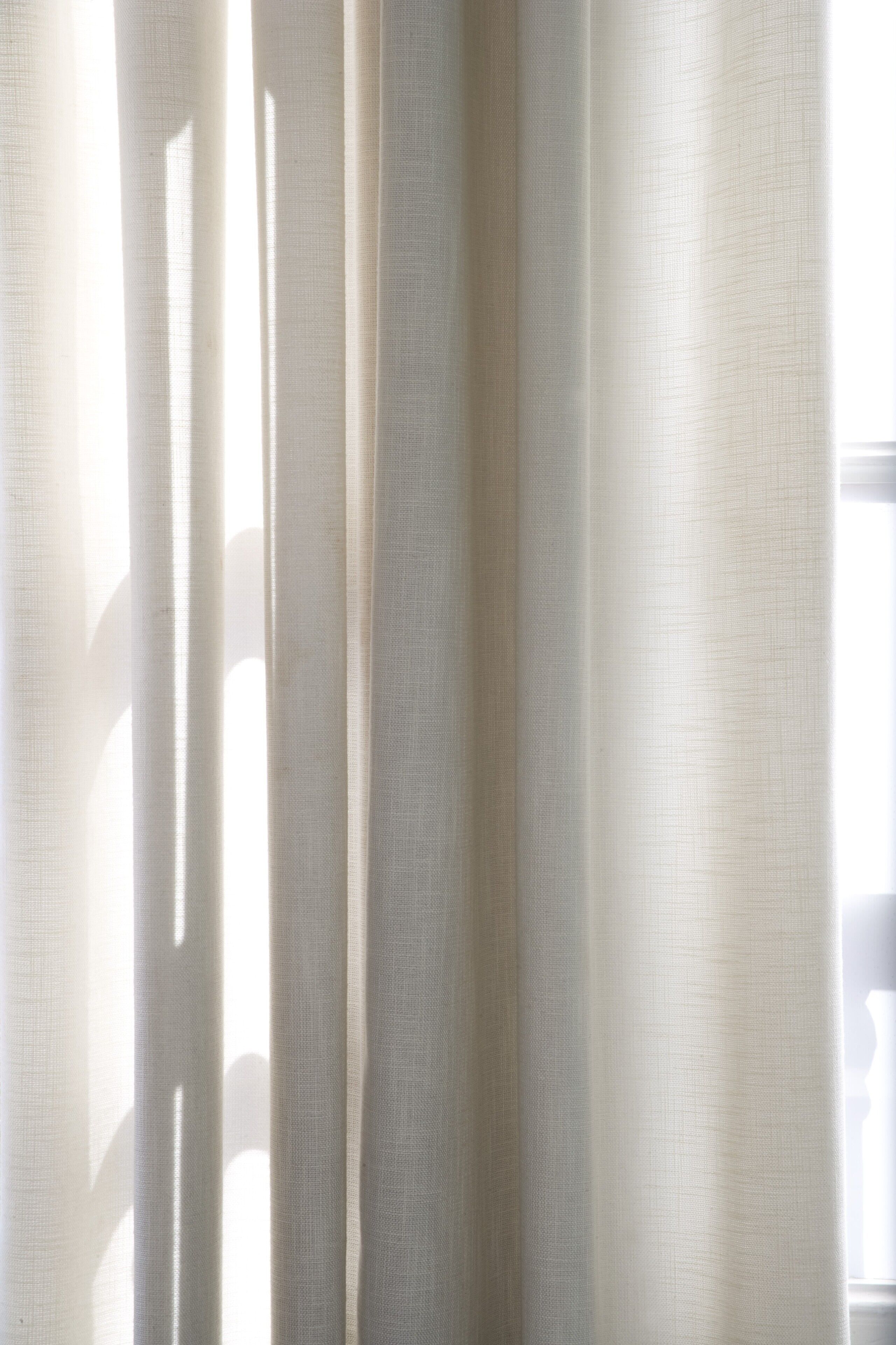 A view of sheer curtains with vertical lines, allowing light to pass through.