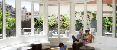 A modern interior with a white sofa, round tables, and large windows offering a view of the city.