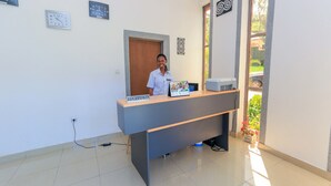 Un mostrador de recepción con un cartel que dice "RECEPTION", un reloj y una ventana con vista a la vegetación exterior.