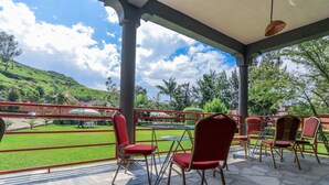 Un espacio de estar al aire libre techado con sillas rojas y una mesa de vidrio, con vistas a un paisaje verde y una colina.
