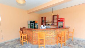 Una zona de bar con mostrador de ladrillo, sillas de madera y estanterías llenas de licores.
